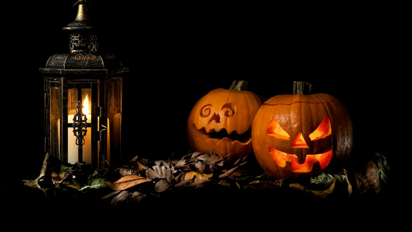 Two carved pumpkins next to a lantern