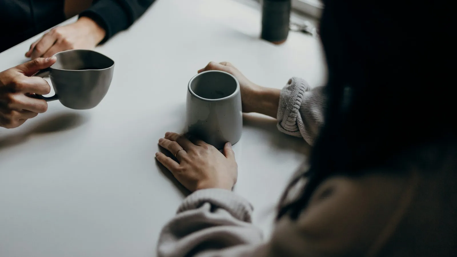 Two people holding mugs across a table