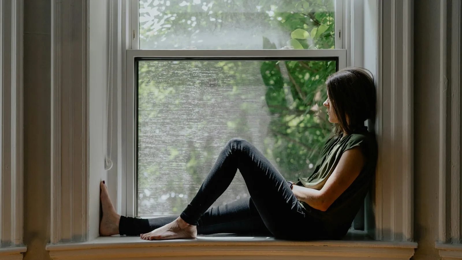 A woman sitting quietly on a window sill